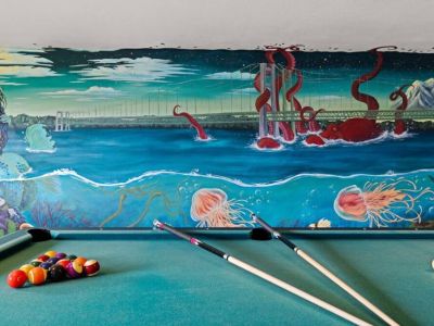 This local artist's hand painted vibrant wall mural transforms this game room space into a masterpiece. Featuring the Narrows Bridge along with iconic Pacific Northwest (PNW) sea life such as the Great Pacific Octopus that she painted as larger-than-