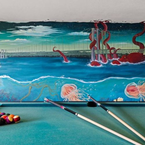 This local artist's hand painted vibrant wall mural transforms this game room space into a masterpiece. Featuring the Narrows Bridge along with iconic Pacific Northwest (PNW) sea life such as the Great Pacific Octopus that she painted as larger-than-