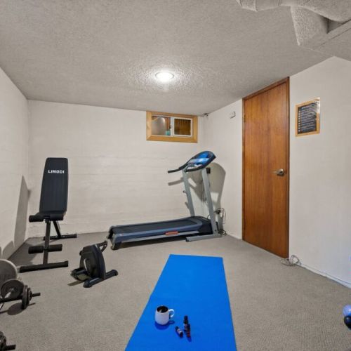 Achieve your fitness goals in the convenience of your home with this well-equipped lower-level gym area, featuring a treadmill, weight bench, and a set of dumbbells.